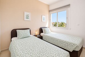 A twin room with two beds, a nightstand, a lamp, and a window with a view of palm trees. - Narcissos Villa 2 - Three Bedroom Villa, Sleeps 8 (Protaras)