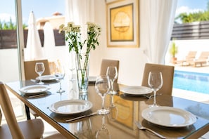 A dining table set for four with white plates, wine glasses, and a vase with white flowers.