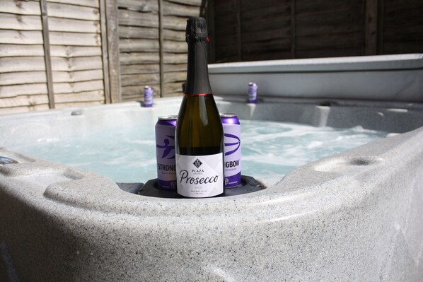A hot tub with a bottle of Prosecco and two cans of GBUW cider.