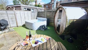 A wooden table with a bottle of wine, glasses, and a plate of grapes and fruit. - Holiday home hot tub and sauna (Bournemouth)