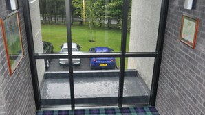 Una habitación con piso a cuadros, vista de coches estacionados afuera y una pared de ladrillo.