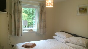 Un dormitorio con cama, almohadas blancas, ventana con cortinas, lámpara de noche y un cuadro enmarcado en la pared.