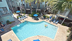 A rooftop pool with lounge chairs and umbrellas, surrounded by a multi-story building with balconies. - 👣 Come get your toes in the sand ~~~ and a cold drink in your hand! 🍹 (Gulf Shores)