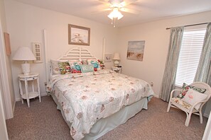 A bedroom with a bed, a chair, a nightstand, a lamp, and a ceiling fan.