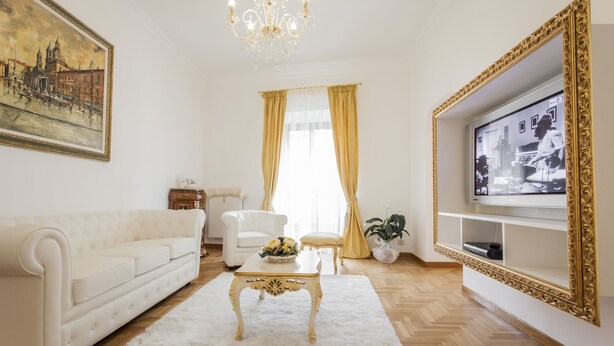 A living room with a white sofa, a gold-framed TV, a chandelier, and a painting on the wall. - Holiday home 'Suite Sarandrea' in Rome in the Vatican area of San Pietro (Roma)