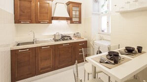 A modern kitchen with wooden cabinets, a stainless steel sink, a gas stove, and a dining area with a table set for two. - Holiday home 'Suite Sarandrea' in Rome in the Vatican area of San Pietro (Roma)