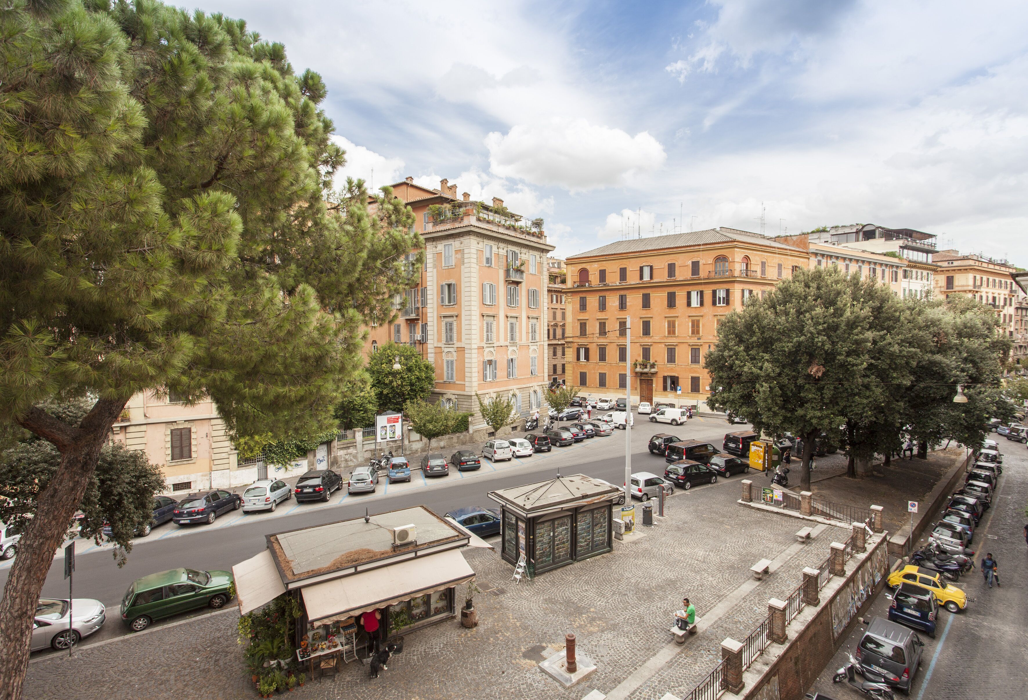 A street view with parked cars, a bus stop, and buildings with balconies.