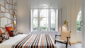 A modern bedroom with a large bed, a chair, and a view of the city through large windows. - Moraza Suite by FeelFree Rentals (San Sebastián)