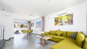 Una sala de estar moderna con un sofá verde, una mesa de centro de madera y un cuadro que representa un paisaje forestal.