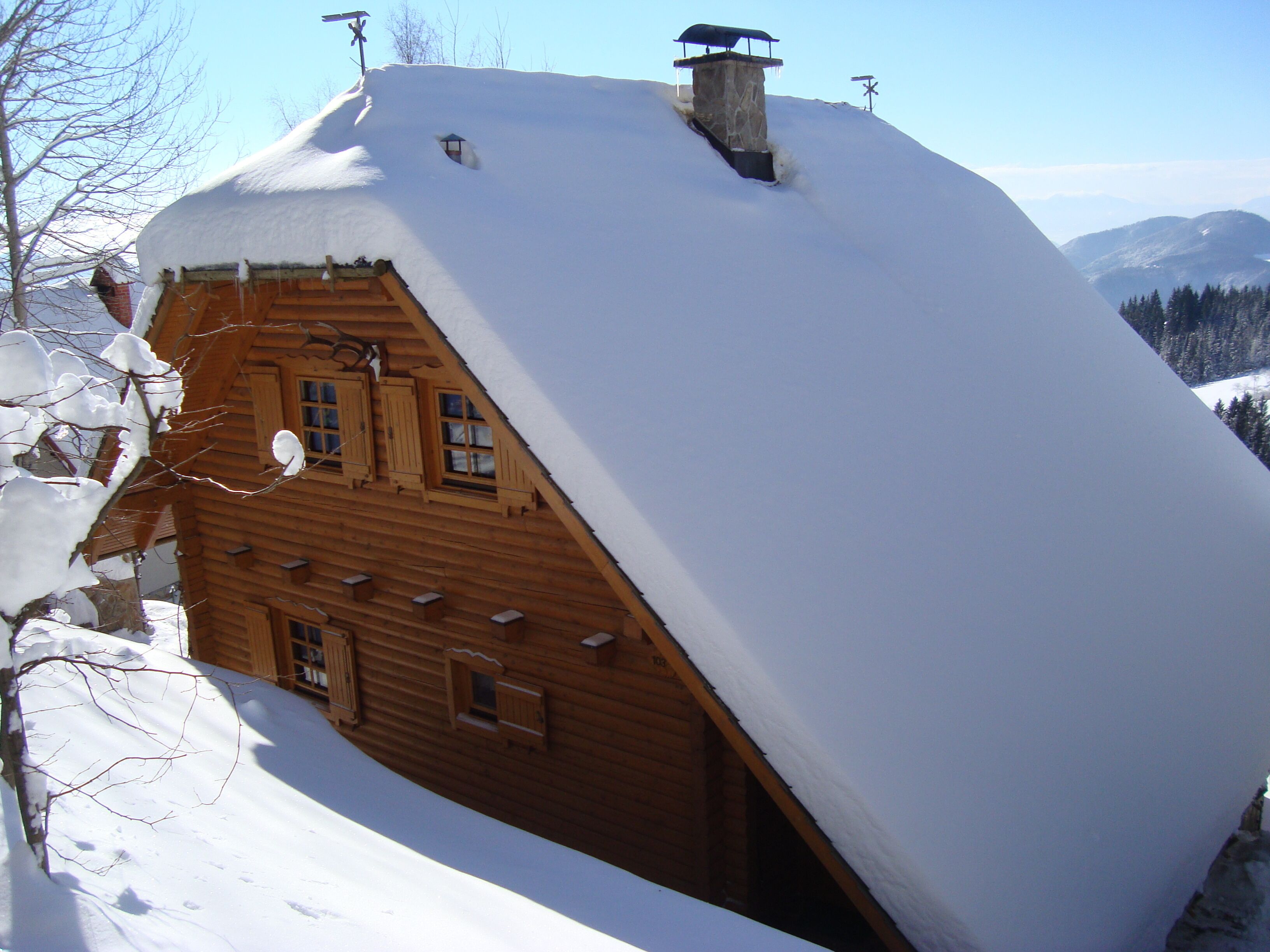 A snow-covered wooden cabin with a steep roof, a chimney, and a small window.