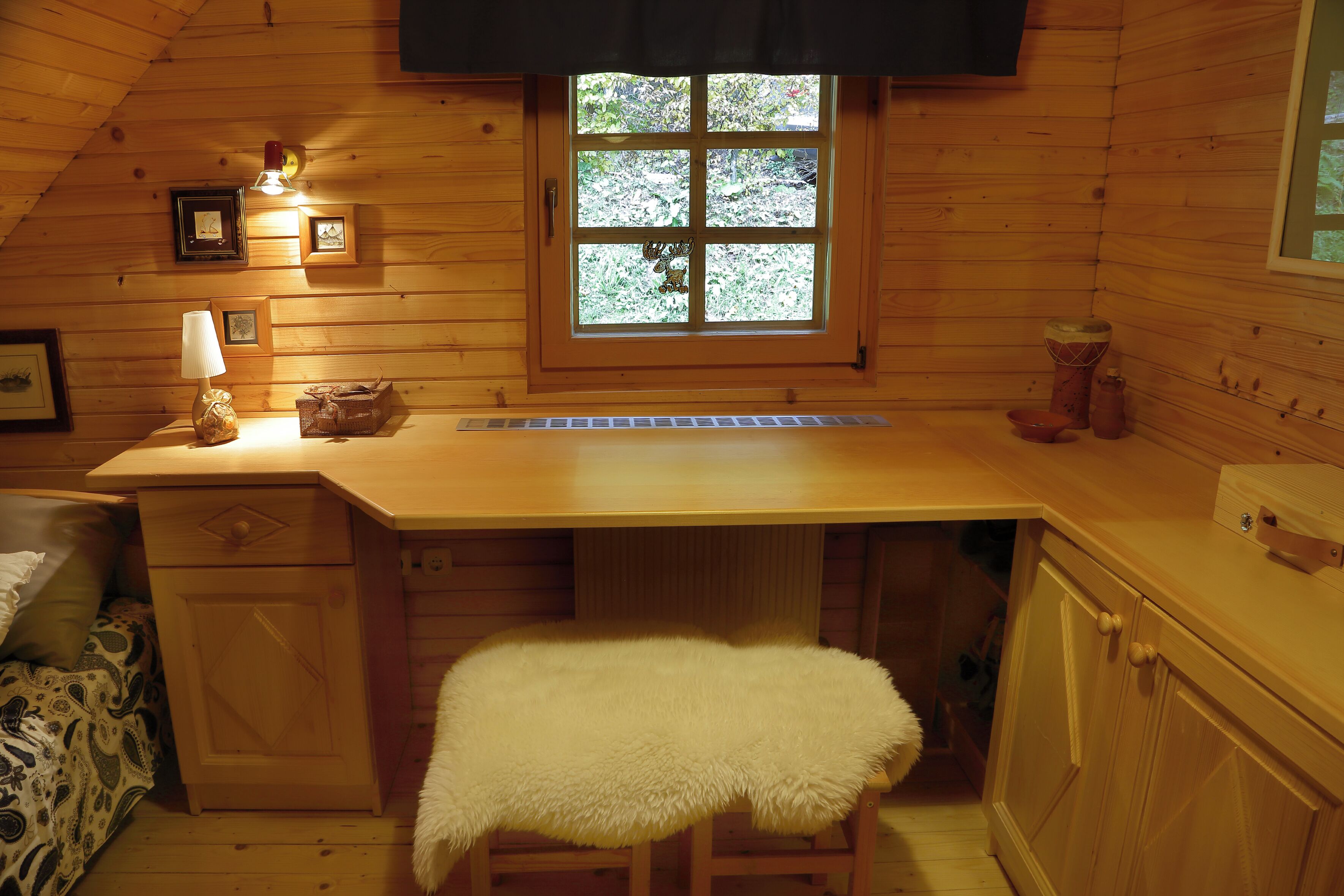 A cozy cabin interior with a wooden desk, a bench, a window with a view, and a small kitchenette area.