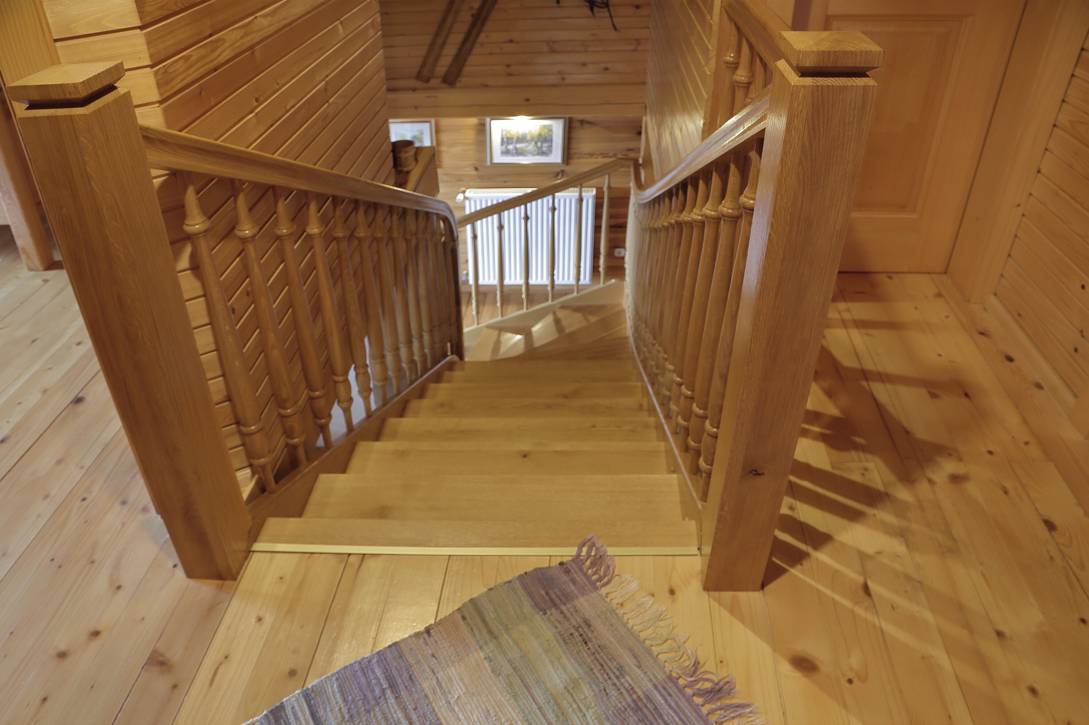 A wooden staircase with a handrail, leading to a landing with a view of the outside.