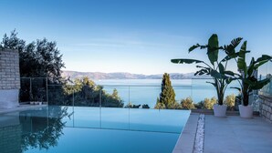 Una piscina moderna d'hidromassatge infinit amb una vista despejada del mar i les muntanyes.