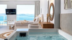 Habitació d'hotel moderna amb un llit gran, zona de seients, banyera i televisió que mostra un programa.