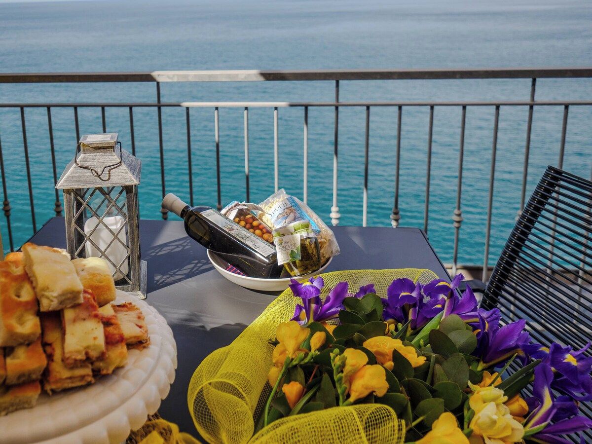 Une table avec de la nourriture et des fleurs sur un balcon donnant sur la mer.