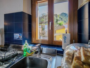 A kitchen with a sink, a dish rack, a window with a view of a building and hills, and a mug with the word 'smile' on it. - La Lampara Sea View Terrace Apartment with AC (Manarola)