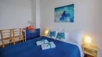 A hotel room with a bed, two chairs, a small table with a vase, and a painting on the wall.