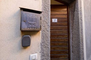A mailbox labeled "POSTA" mounted on a textured wall, a door with a wooden panel, and a small sign above the door.