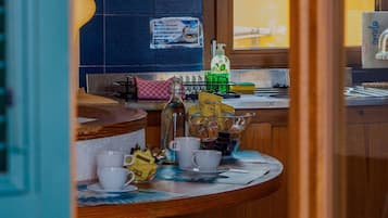 A kitchen area with a tiled backsplash, a window with a view, a sink, and a countertop with various items including a bottle, cups, and a bag of snacks.