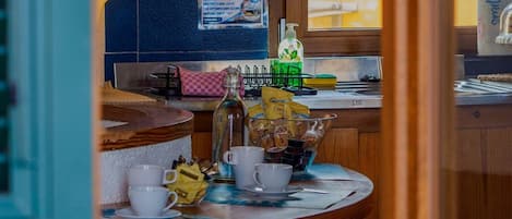 A kitchen area with a tiled backsplash, a window with a view, a sink, and a countertop with various items including a bottle, cups, and a bag of snacks.