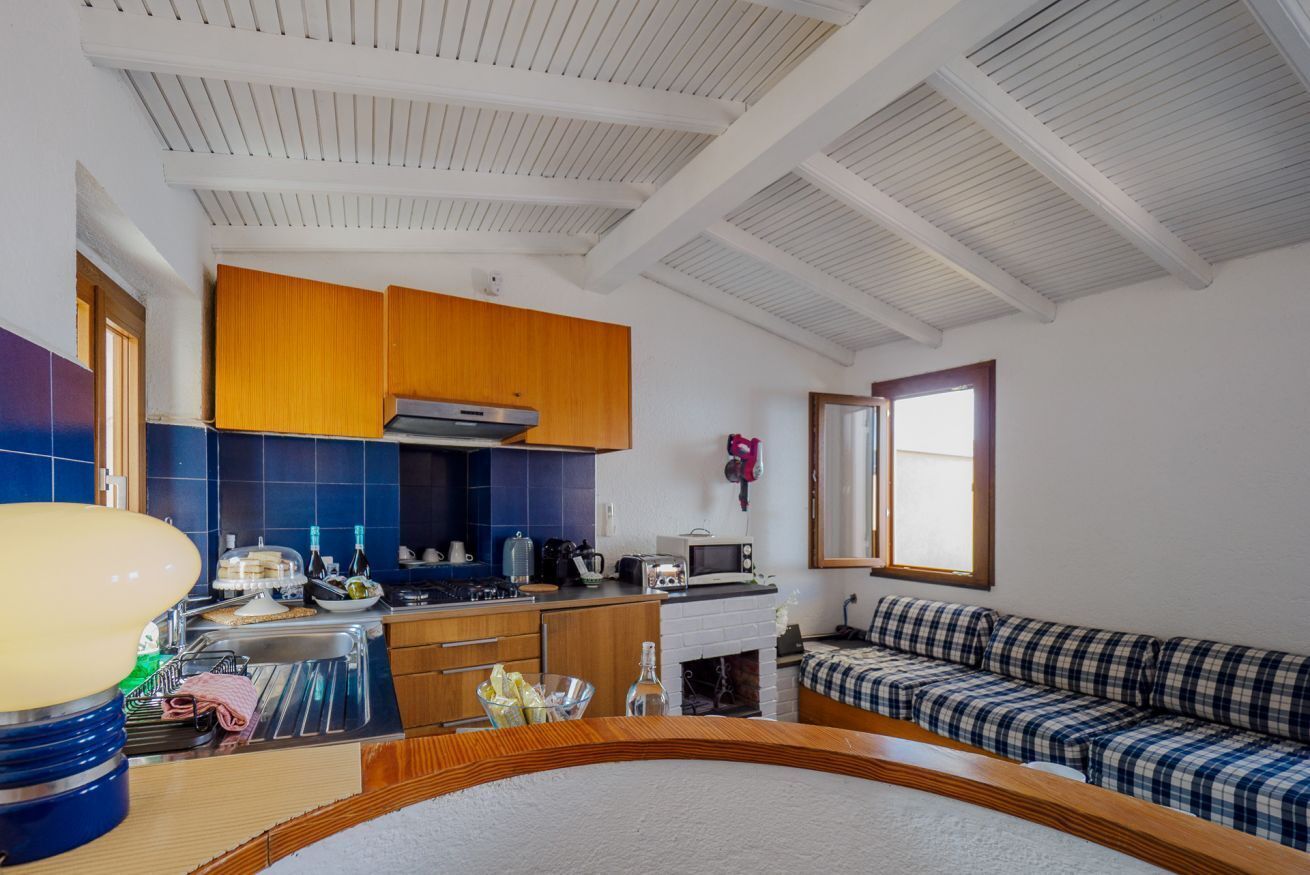 A compact kitchen with wooden cabinets, a built-in stove, and a microwave. There is a window providing natural light and a sofa in the adjacent living area.