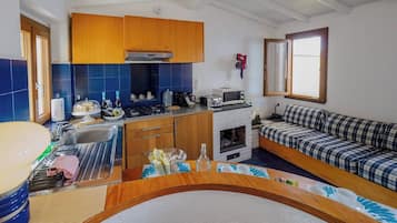 Ett kompakt kök med en inbyggd spis, en mikrovågsugn och en liten matplats med en soffa i rutmönster.