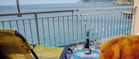 Un balcon avec vue sur la mer, une table avec une bouteille et des verres, et une chaise jaune.