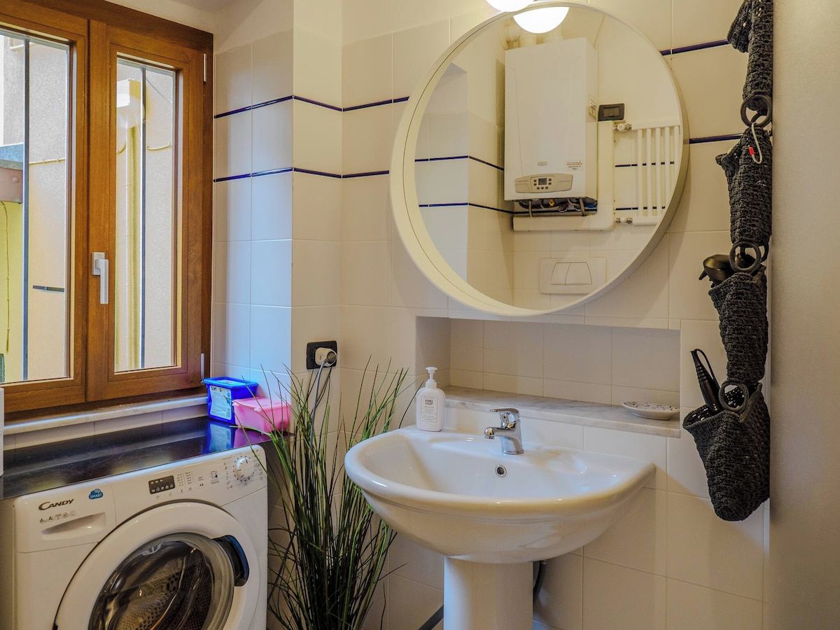Une petite salle de bain équipée d’un lave-linge, d’un évier et d’un miroir.