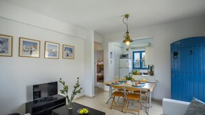 A living room with a TV, a dining area with a table and chairs, and a kitchen visible through an open door. - Protaras Ayios Elias Suite (Protaras)