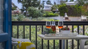 A balcony with a table holding two bottles and glasses, a bowl of strawberries, and a tray with a plant. - Protaras Ayios Elias Suite (Protaras)