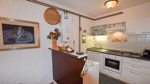 Eine Küche mit weißen Schränken, einer Spüle, einem Backofen und einem Herd. An der Wand hängt ein gerahmtes Bild und auf der Arbeitsfläche steht ein Korb.