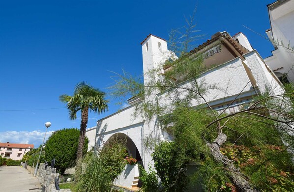 A white building with a bell tower, surrounded by greenery and a clear blue sky.