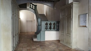 A hallway with a tiled floor, a staircase with a balustrade, and a door with a bulletin board. - 10' from St Rémy and Avignon, charming apartment ***, 2 bedrooms for 4 people (Noves)