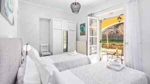 A hotel room with two beds, a desk, a chair, and a view of the outdoor area. - Villa Secret Paradise (Corfu)