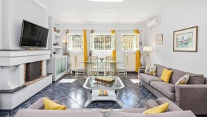 A living room with a flat-screen TV, a glass-top coffee table, a sofa, and a dining area with a table and chairs. - Villa Secret Paradise (Corfu)