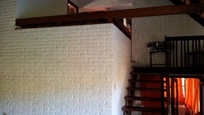 Una scala con ringhiere in legno conduce a una stanza con un muro in mattoni e una finestra con tende arancioni.