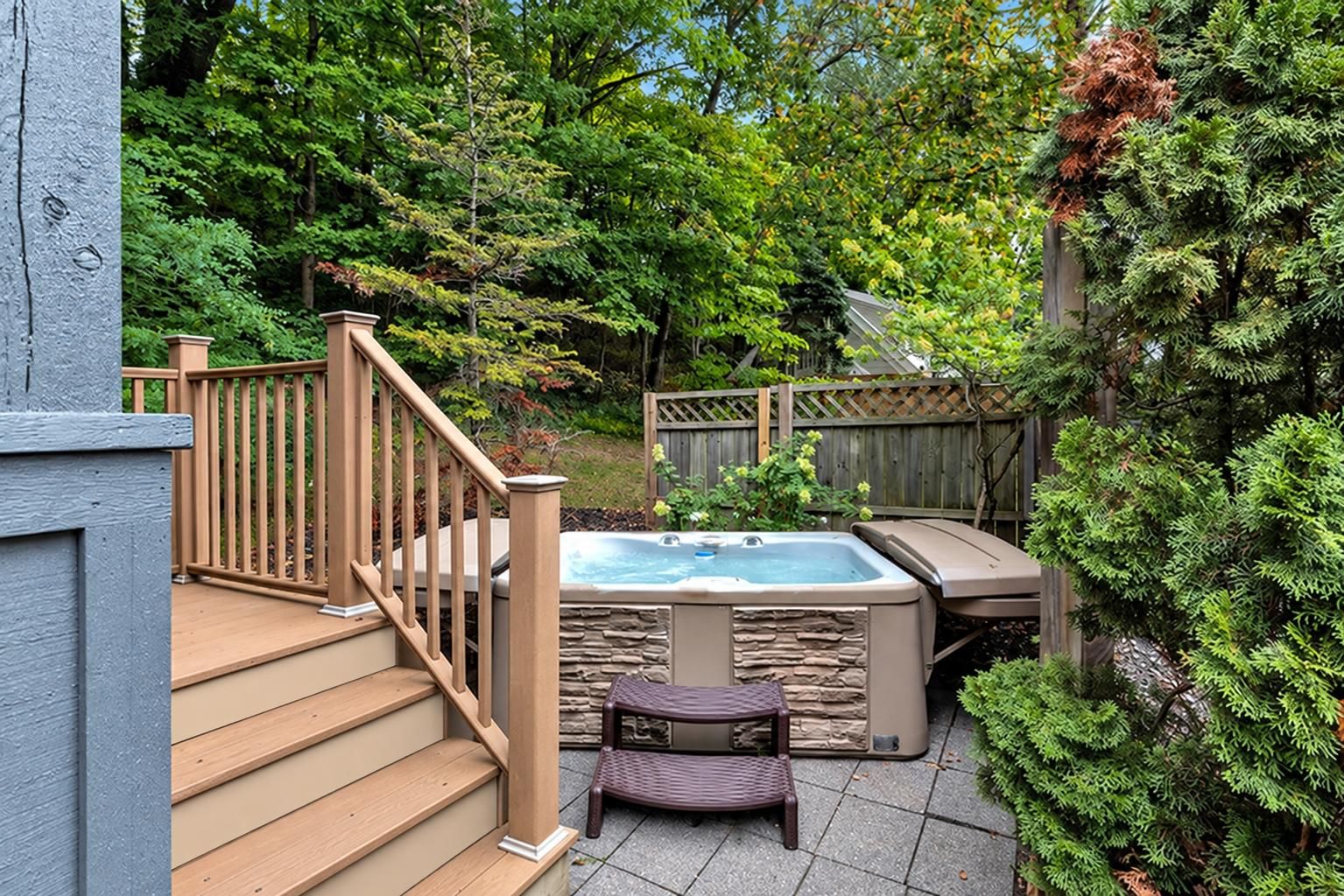 A hot tub in a backyard with wooden stairs and a deck.