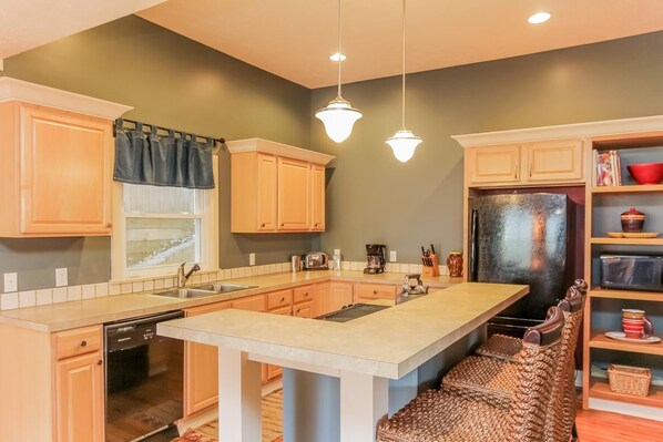 A kitchen with wooden cabinets, a central island, a refrigerator, and hanging pendant lights.