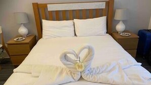 A neatly made bed with a heart-shaped towel arrangement in the center, wooden headboard, white bedding, and bedside lamps on wooden nightstands. - Bournemouth hot tub and sauna holiday let (Bournemouth)
