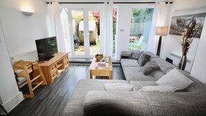 A modern living room with a grey sofa, wooden coffee table, and a television on a wooden stand. - Bournemouth hot tub and sauna holiday let (Bournemouth)