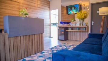 Uma área de recepção moderna com um balcão de madeira, um sofá azul, um tapete estampado e uma televisão fixada na parede.
