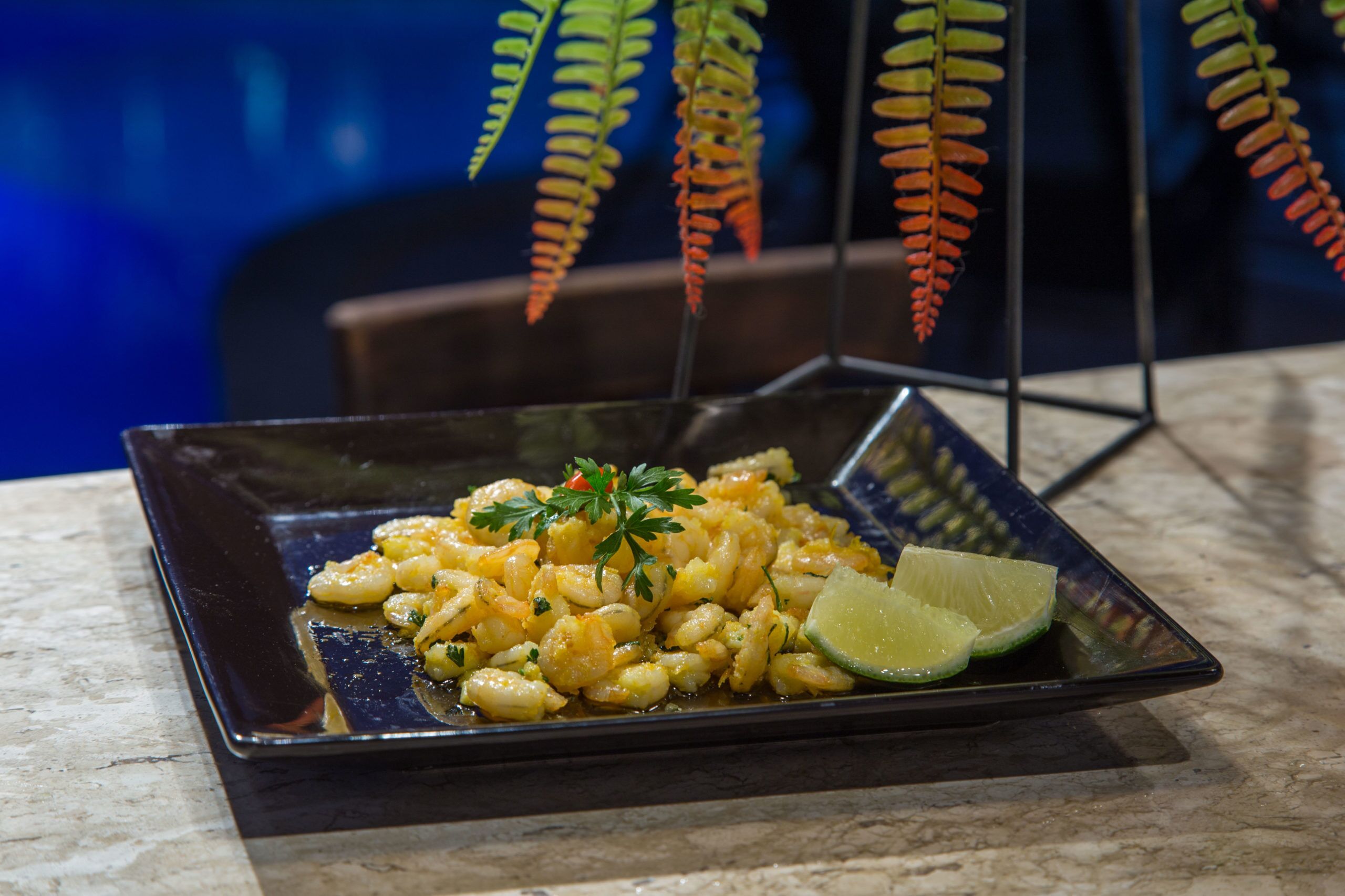 Un plato cuadrado con un plato de mariscos, adornado con perejil y una cuña de lima sobre una encimera de mármol.