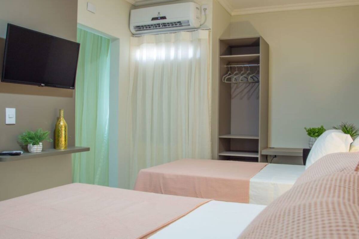Habitación de hotel con dos camas, televisión, aire acondicionado, armario y una planta pequeña.
