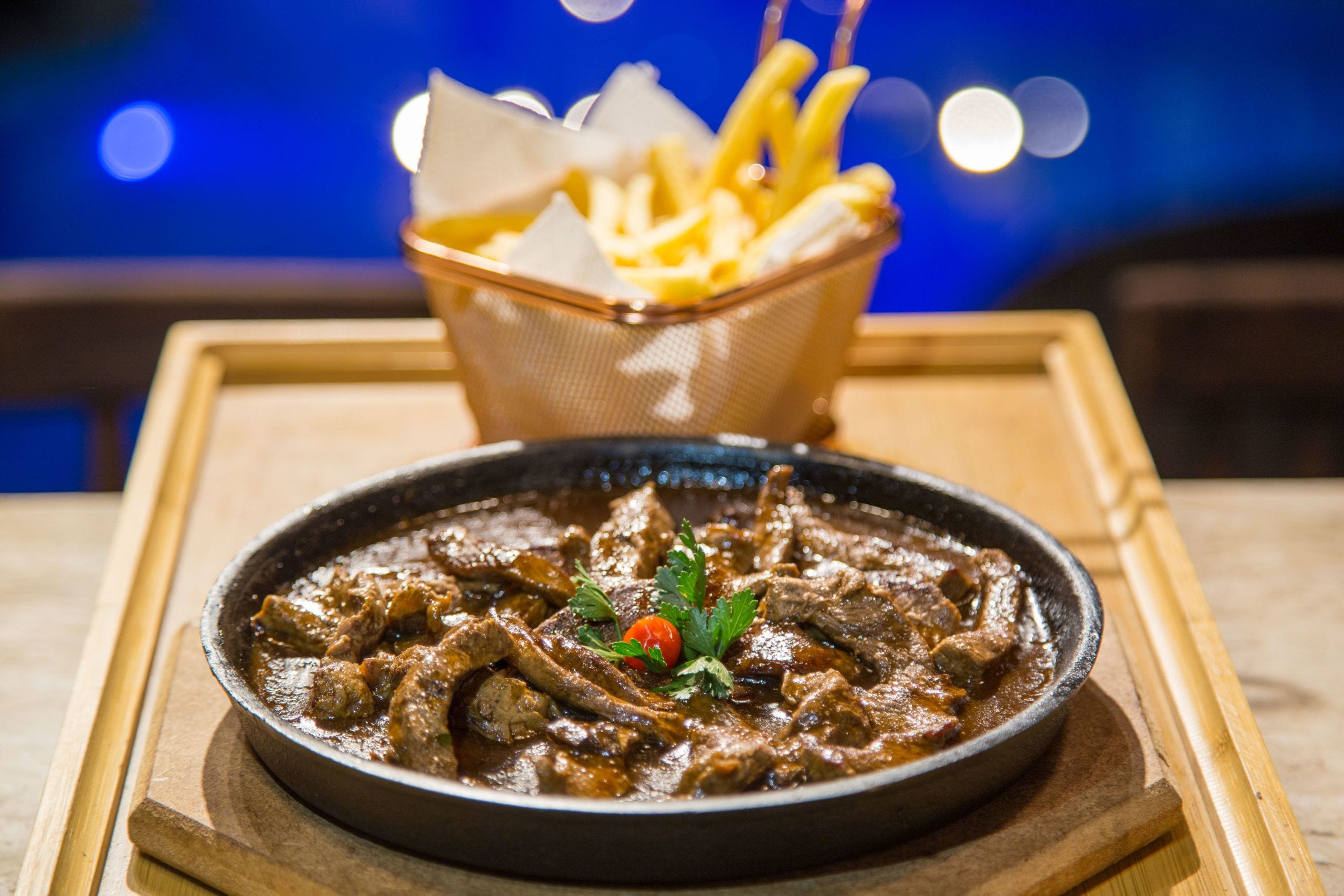 Un plato de estofado de carne con guarnición, servido sobre una bandeja de madera.