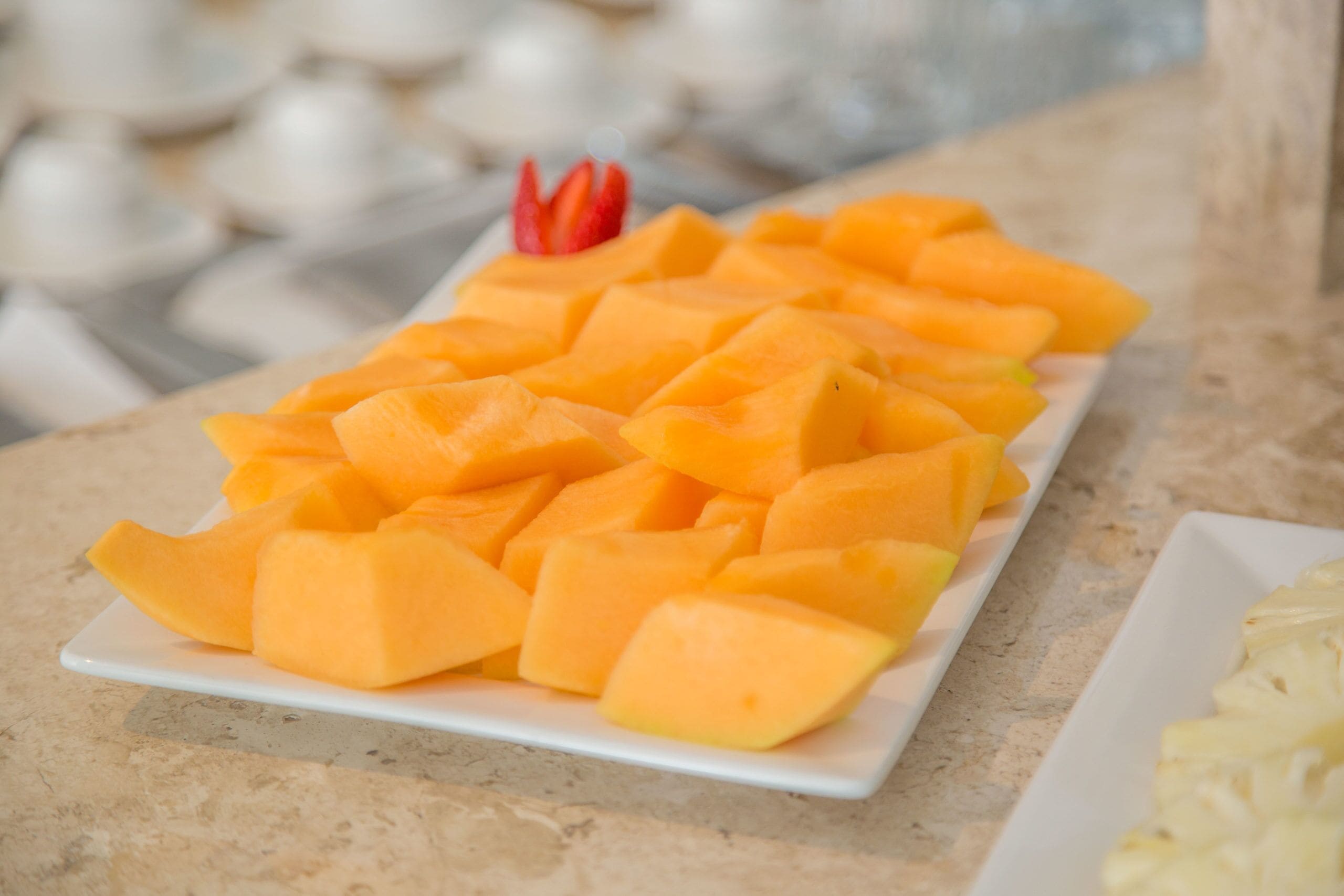 A white rectangular plate filled with cubed mangoes and a few red strawberries on a marble countertop.