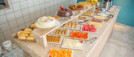 Un bufé con diversas opciones de comida, incluyendo pasteles, productos de pastelería, frutas y bebidas.