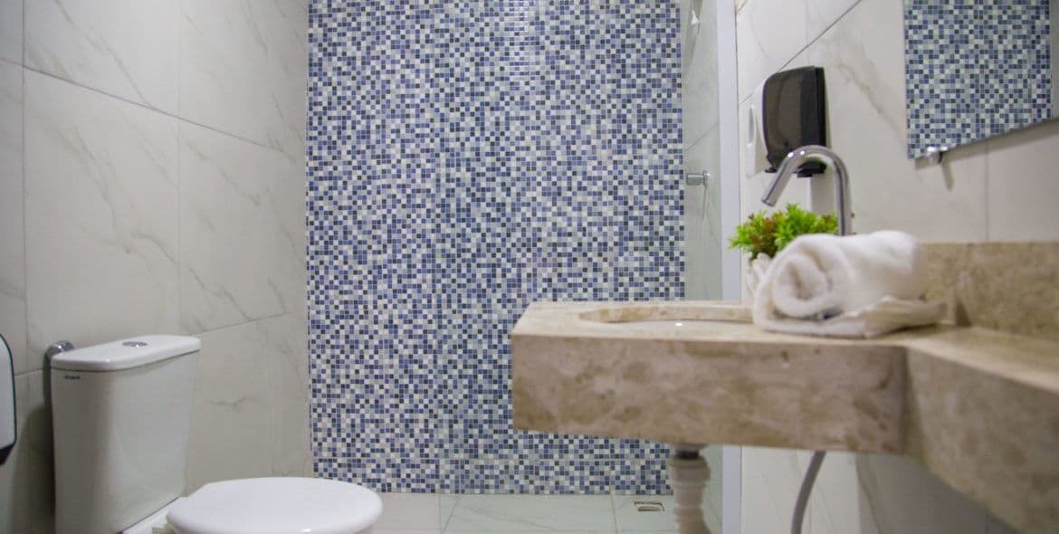 A bathroom with a toilet, a sink with a towel, and a shower area with mosaic tiles.