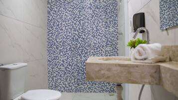 Un baño con inodoro, lavamanos con una toalla y zona de ducha con mosaicos.