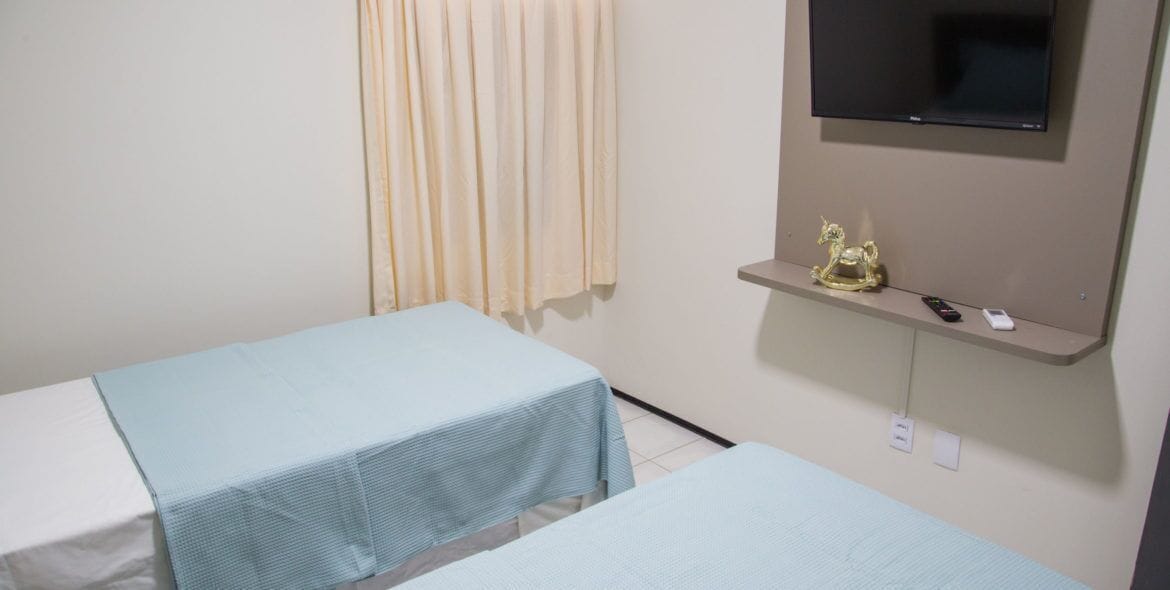A room with two single beds, a television mounted on the wall, and a small shelf with a decorative item.