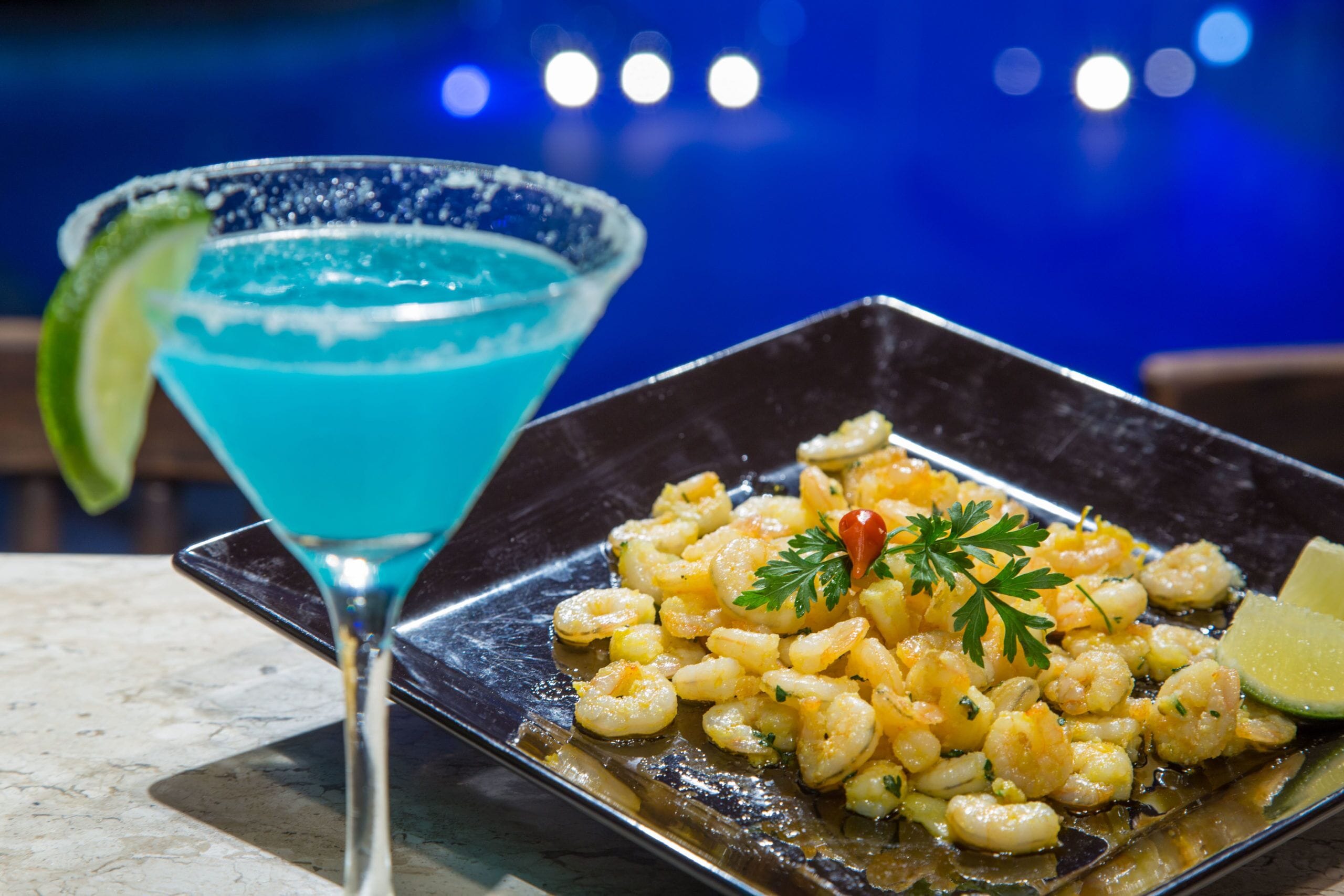 A plate of shrimp with garnish and a blue cocktail with a lime garnish.